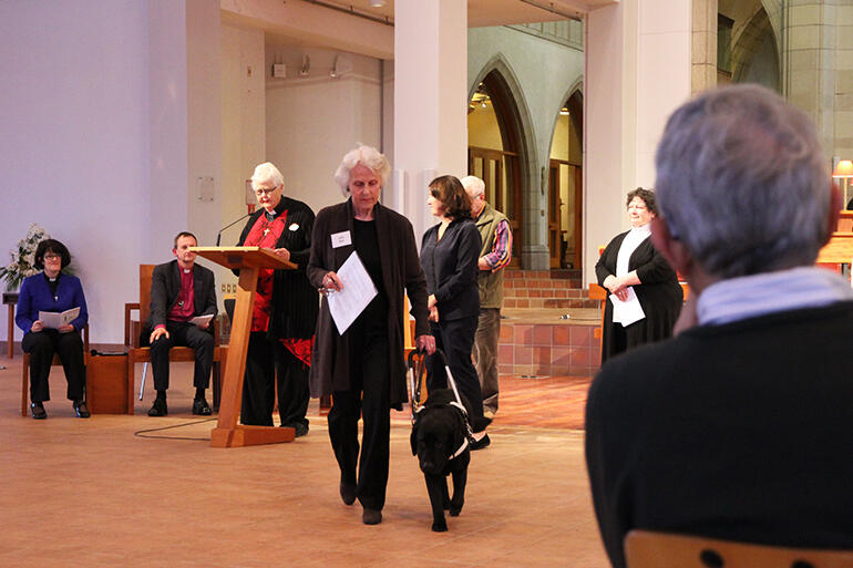 Julie Bull, who is on the pastoral care team at St Aidan's, Remuera, returns from the lectern to her seat with the help of her guide dog.