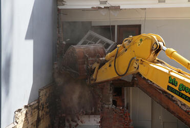 The jaws of the digger rake out a window at the back of Statham.