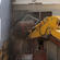 The jaws of the digger rake out a window at the back of Statham.