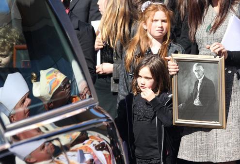One of Sir Paul's mokopuna watches as lies in the hearse. Archbishops Moxon and Sentamu are reflected in the hearse window.