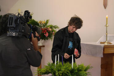 Under the scrutiny of the TV cameras, young Joshua Copp lights the first Advent candle at the Cobden Church.