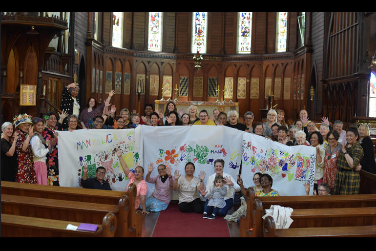 2023 Anglican Women's Studies Hui members gather round their banners depicting hui theme: 'Many Hands'.