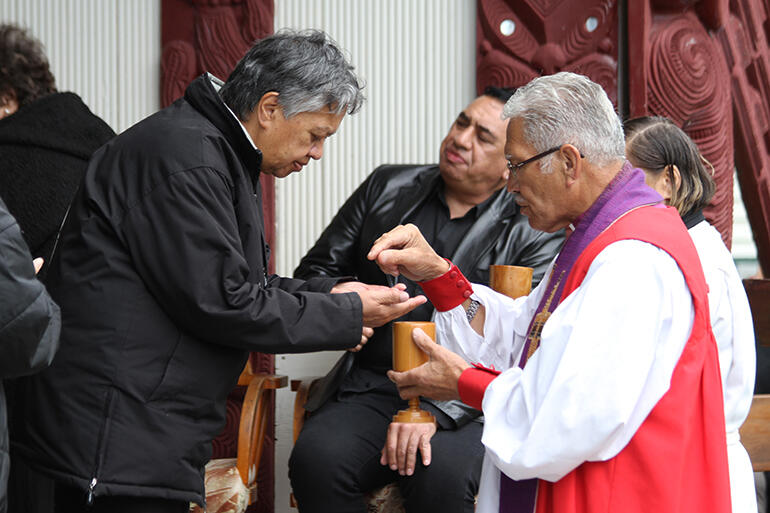 Bishop Ngarahu Katene serves the Eucharist wafer to Lorraine Toki.