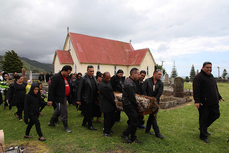 The pallbearers carry Bishop John through Tuatini urupa, with St Mary's Anglican church in the background.