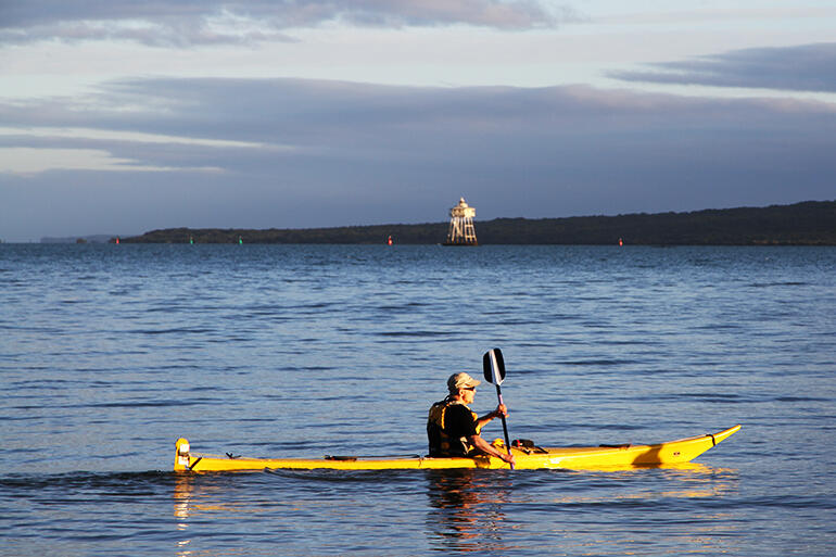 The early morning sun catches Bishop Jim as he glides his kayak in front of the Bean Rock lighthouse.