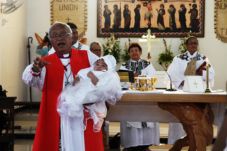 Archbishop Winston speaks to the congregation - while holding Robert Guy Sullivan, the first child to be baptised in the reborn church.