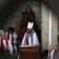 Archbishop Winston seated in his cathedra - as seen through the masonry grill of the mezzanine gallery.