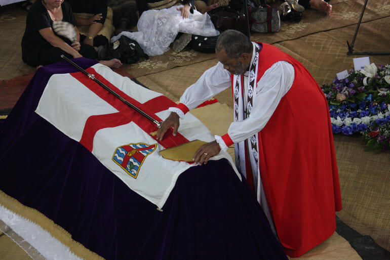 Bishop Api Qiliho lays the Archbishop's mitre and crozier on the casket. 
