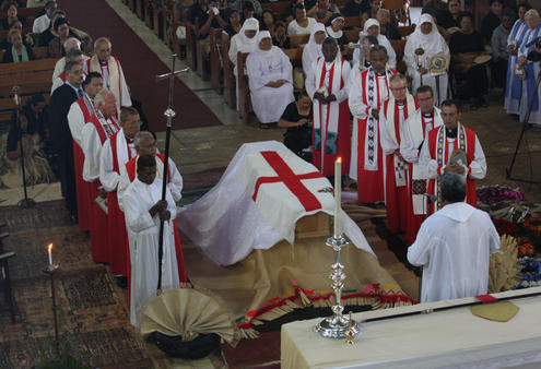 The Archbishop has just been brought into the cathedral, and Dean Cama is inviting mourners to file past the coffin.