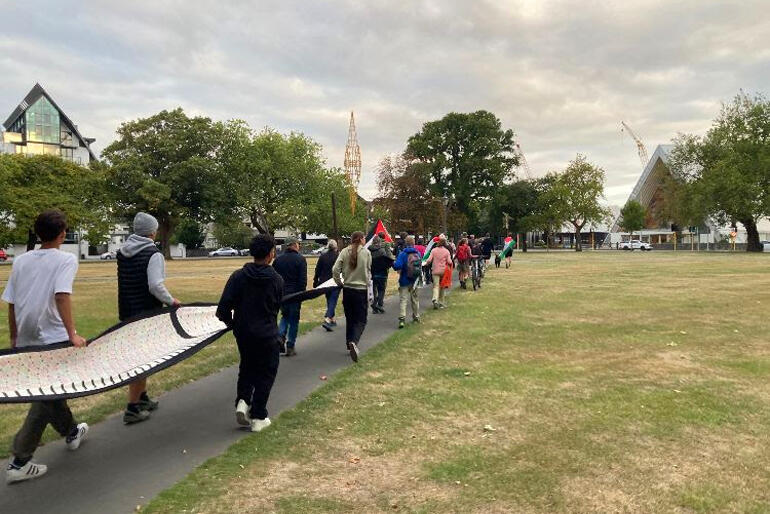 A line of pilgrims walk towards Christchurch's Transitional Cathedral as evening falls on the Gaza Ceasefire Pilgrimage on 9 March 2024.