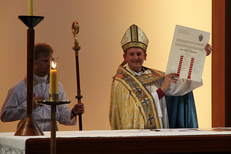 Mission accomplished: a jubilant Bishop Ross Bay holds aloft the Consecration Charter he's just signed.