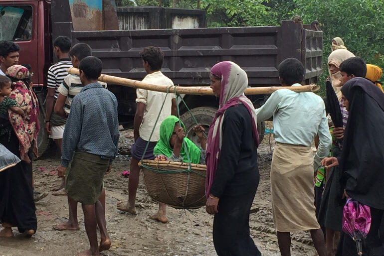 A Rohingya family flees on foot carrying an elderly relative. Photo:Christian Aid. A Rohingya family flees on foot carrying an elderly relative. Photo:Christian Aid.