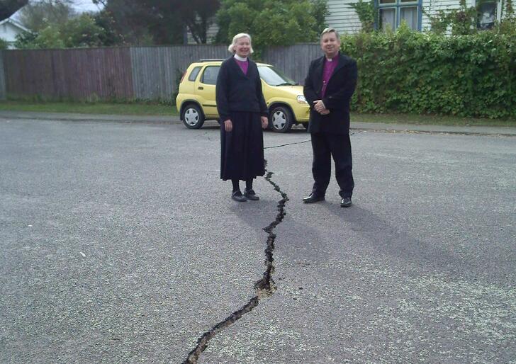Bishop Victoria and Archbishop David stand either side of the rift in the road outside Churchill Courts' aged care complex.