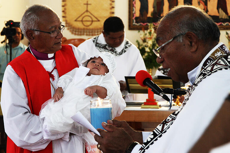 The Archdeacon of Tonga, Fr Joe Le'ota, prepares to present a baptismal candle to baby Robert's family.