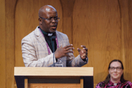 Zambian ACC delegate Archdeacon Bob Sihubwa speaks at a podium as Bishop Eleanor Sanderson looks on