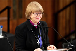 Archbishop of Canterbury Sarah Mullally stands at a lectern with a pleasant expression
