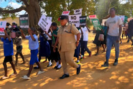 Young Malawi Anglicans walk in a sunny red-earthed street with placards "No Planet B" and Reduce, reuse, recycle"
