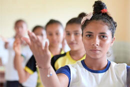 A dark-haired teenaged girl raises her hand in a dance gesture 