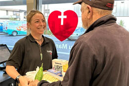A woman smiles as she hands a food box to an older man