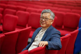 A Chinese priest in a clerical shirt sits in a meeting hall