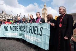 Clergy line up with protestors behind a banner reading "No more fossil fuels"