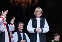 Bishop Sarah Mullally stand against a black background as bishops' hands applaud her confirmation