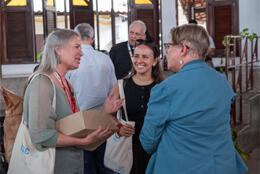 Three women stand smiling and talking in a meeting hall