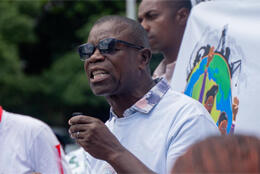 A middle-aged African man speaks in a group with the earth on their t-shirts