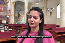 A Palestinian teenaged girl in a pink jumper talks stands in Gaza church as people decorate for Xmas