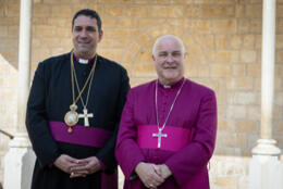Archbishops of York and Jerusalem stand together in purple cassocks against a gold stone wall