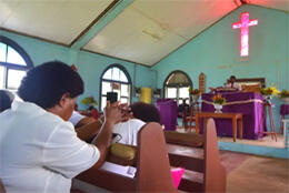 Fijians sit in a sun-drenched painted concrete church
