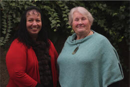 Two women smile at the camera against an ivy covered wall