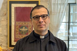 Palestinian Reverend Isaac Munther smiles gently in a room with Christian tapestries