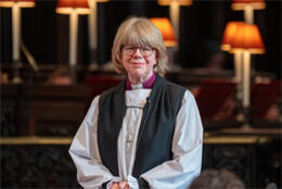 Bishop Sarah Mullally stands in black stole & white rochet against a background of choir lights