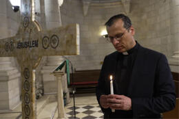 A Palestinian Lutheran pastor lights a candle in a stone church next to a cross inscribed with the word Jerusalem