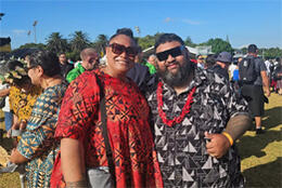 Melvina Martin and Nathan Lopa in bright Pacific print clothes stand smiling in a sunny Auckland field 