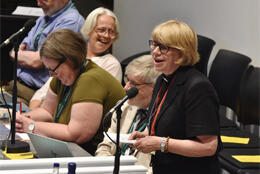 Archbishop of Canterbury Sarah Mullally stands at a podium smiling as others laugh in the background