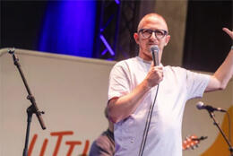 Rev Scottie Reeve in a T-shirt waves from onstage in