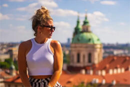 A blond woman stands above a European city scape with a large church dome at the centre
