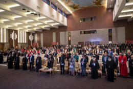 100s of diverse church people stand in a huge room with angels painted on the ceiling