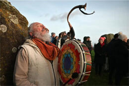 A grey-bearded man looks towards the sky holding a patterned drum