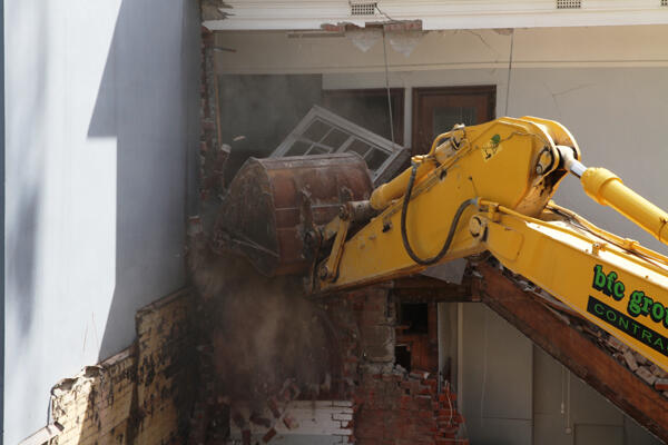 The jaws of the digger rake out a window at the back of Statham.