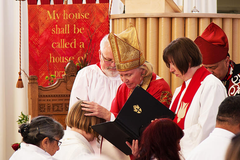 Bishop Victoria lays hands on Carolyn Robertson. That's the Rev Jenny Wilkens with the book.