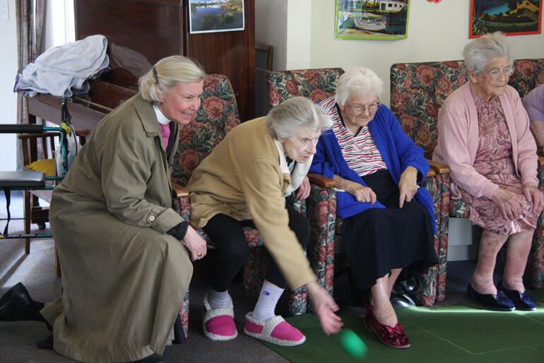 Bishop Victoria watches while a spirited game of indoor bowls is in progress.