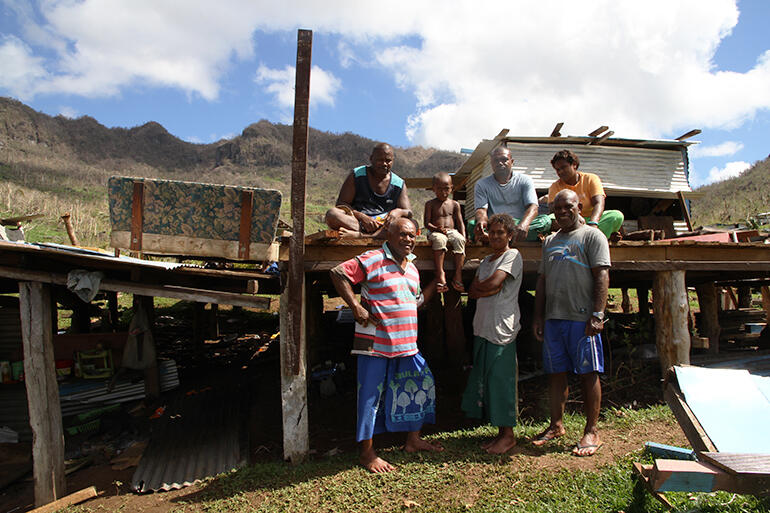 Mosese Kakaramu (in the striped jersey) stands in front of his basement, where his family rode out the cyclone which destroyed his two storey house.