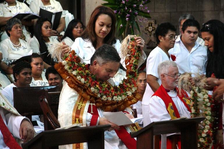 Archbishop David bows his head as he is wreathed in a Pacific garland.