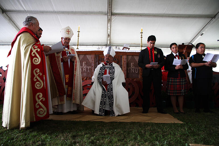 The two other pihopa present and the three students surround the archbishop (who is seated on his cathedra) in prayer.