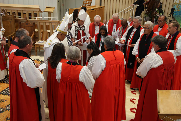 Bishop-elect Susan Wallace kneels as the bishops gather in prayer and Hukarere students sing a waiata invoking Te Wairua Tapu.