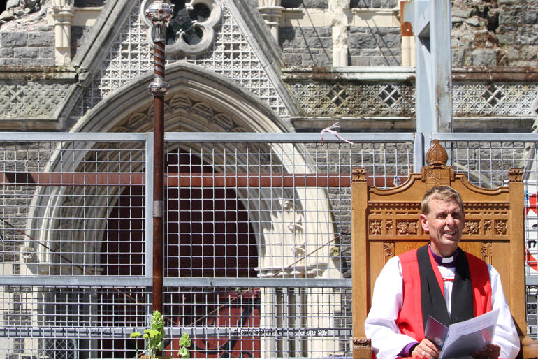 Bishop Peter sits in his cathedra – outside the cordon – and in view of the doors of his ruined cathedral.