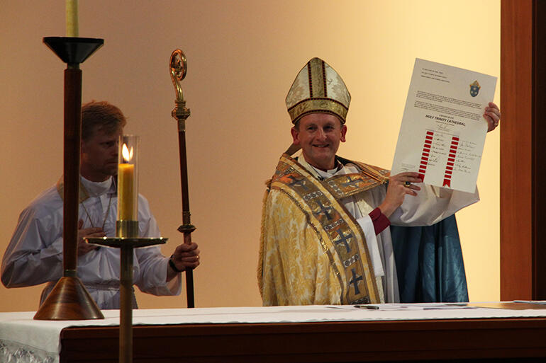 Mission accomplished: a jubilant Bishop Ross Bay holds aloft the Consecration Charter he's just signed. Mission accomplished: a jubilant Bishop Ross Bay holds aloft the Consecration Charter he's just signed.